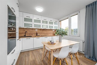 Moderní kuchyň s dřevěnou podlahou, vestavěnými spotřebiči a velkými okny zajišťujícími dostatek světla.