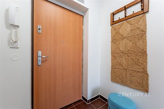 Vstupní chodba s dlažbou a dřevěnými dveřmi, obsahuje interkom a věšák na oblečení, moderní styl.