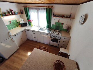 Kuchyň s dřevěnou podlahou, moderními skříňkami a velkými okny. Světlá prostorová dispozice s praktickou pracovní deskou.