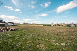 Prázdná stavební parcela s udržovaným trávníkem, na okraji klidné vesnice, ideální pro výstavbu, obklopená venkovskou krajinou