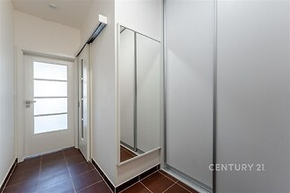 Úzká chodba s dlažbou, velkým zrcadlem a posuvnými dveřmi. Moderní design s čistými liniemi a světlými stěnami.