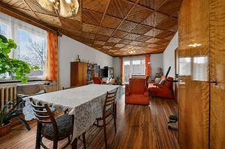 Prostorný obývací pokoj s dřevěným stropem, světlá parketová podlaha a velká okna, vybavený retro nábytkem, ideální pro modernizaci.
