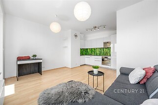 Světlý obývací pokoj s moderní kuchyní, parketová podlaha, vestavěné skříně, světlý interiér, pohodlná pohovka, zelená kuchyňská zástěna.