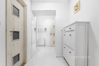 Úzká bílá chodba s dlažbou, moderními dveřmi a vestavěnou skříní, která nabízí prostorný a světlý vstupní prostor.