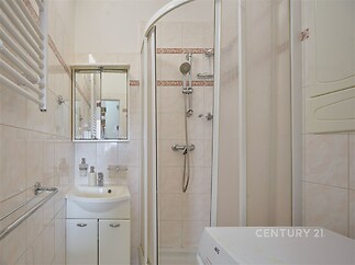 Kompaktní koupelna s dlažbou, sprchovým koutem a moderními úložnými skříňkami, ideální pro malé byty nebo rekreační objekty.