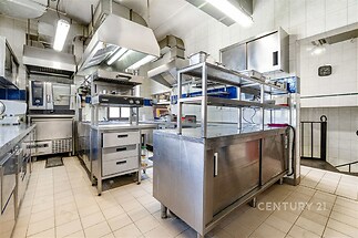Profesionální kuchyň s nerezovým vybavením, dlažbou a velkým oknem zajišťujícím světlost, ideální pro gastronomický provoz.