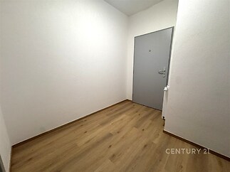 Úzká předsíň s dřevěnou podlahou, bílými stěnami a moderními šedými dveřmi, vyniká svou jednoduchostí a čistým designem.