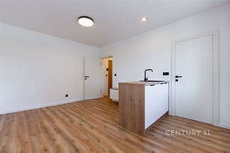 Kuchyňský kout s moderními dřevěnými dvířky, parketová podlaha, světlý interiér s minimalistickým stylem a vestavěným osvětlením.