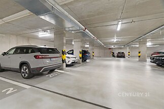 Podzemní garáž s osvětlením, betonovou podlahou a označenými parkovacími místy, moderní zabezpečení a snadný přístup pro rezidenty.