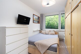 Prostorná ložnice s vestavěnými skříněmi, velkými okny a moderním nábytkem, světlý interiér s výhledem do zeleně.