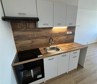 Moderní kuchyň s dřevěnou pracovní deskou, vestavěnými skříněmi a parketovou podlahou nabízí praktické a stylové řešení pro vaření.