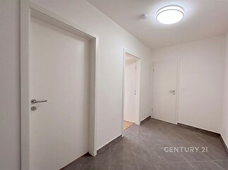 Světlá vstupní hala s moderní dlažbou, bílými dveřmi a čistými liniemi poskytuje elegantní vstup do bytu.