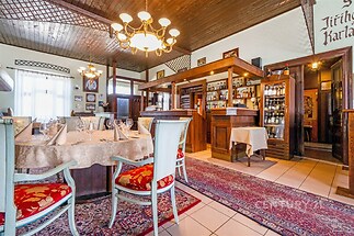 Restaurace ve stylovém interiéru s dekorativními koberci, dřevěným stropem a klasickými židlemi.