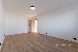 Prázdná světlá místnost s moderní parketovou podlahou, bílými stěnami a dřevěnými dveřmi, ideální pro flexibilní využití a dekoraci.