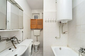 Koupelna s keramickými dlaždicemi, bílými stěnami a plynovým kotlem, zahrnuje umyvadlo, zrcadlovou skříňku a vanu, vhodná k rekonstrukci.