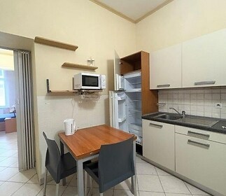 Kuchyň s dlažbou a moderními skříňkami, vybavená vestavěnými spotřebiči a jídelním stolem pro dva, světlý prostor pro praktické vaření.