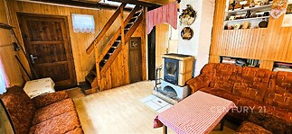 Rustikální obývací pokoj s dřevěným obložením, krbovými kamny a schodištěm, vybavený dřevěnou podlahou a vestavěnými policemi, v útulném stylu.