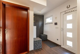 Vstupní hala s dřevěnými dveřmi, moderní podlahou a velkými světlými dveřmi. Úložný prostor je elegantně řešen sedacími boxy.