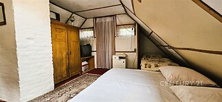 Podkrovní ložnice se starožitnou dřevěnou skříní, velkou postelí a kobercem, nabízí útulný prostor s dobovým nábytkem.