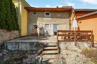 Zahradní terasa s kamennou dlažbou a dřevěným plotem, ideální pro relaxaci. Rustikální fasáda dodává prostoru jedinečný charakter.