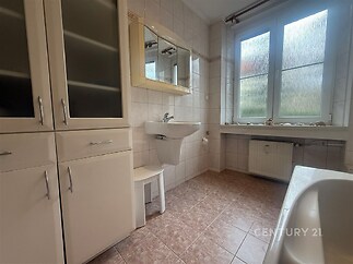 Koupelna s dlažbou a velkými okny zajišťujícími přirozené osvětlení, bílý nábytek v moderním stylu, čistý a udržovaný prostor.