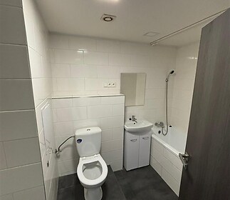 Koupelna s dlažbou, moderní sanitou a klasickou vanou, jednoduché bílé obklady, dobře osvětlená s vestavěným umyvadlem.
