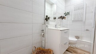 Moderní koupelna s bílými dlaždicemi, stylovým umyvadlem a úložným prostorem, nabízí světlý a čistý design ideální pro komfortní bydlení.