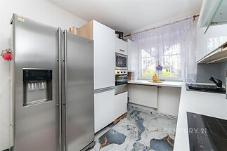 Moderní kuchyň s mramorovou dlažbou, vestavěnými spotřebiči a velkými okny, poskytujícími dostatek světla.