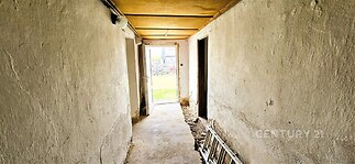 Úzká chodba s neomítnutými stěnami a betonovou podlahou, starší stavba, vyžadující rekonstrukci.