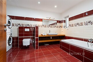 Prostorná koupelna s červenými dlaždicemi, moderní sanitou a vestavěným úložným prostorem, ve výborném stavu, ideální pro rodinné bydlení