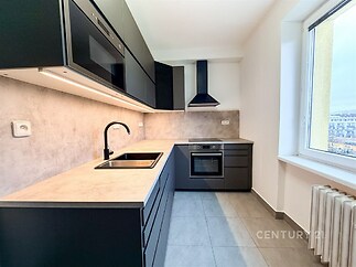 Moderní kuchyň s tmavými skříňkami, vestavěnými spotřebiči a světlou dlažbou, nabízí elegantní design a současné vybavení.