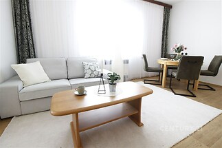 Světlý obývací pokoj s parketovou podlahou, velkými okny a moderním nábytkem.