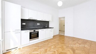 Moderní kuchyň s parketovou podlahou, bílými skříňkami a vestavěnými spotřebiči, světlá místnost s velkými okny a elegantním designem.