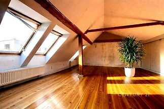 Podkrovní pokoj s dřevěnou podlahou, velká okna a moderní design, světlý prostor ideální pro relaxaci nebo domácí kancelář