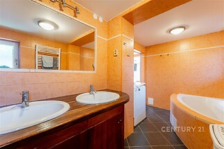 Koupelna s moderním vybavením, dřevěná skříňka pod umyvadly, velké zrcadlo, rohová vana, oranžové obklady, elegantní design