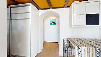 Úzká chodba s moderní vestavěnou skříní a dřevěným stropem, zdobená bílými stěnami a obrázkem, obklopená světlou dřevěnou podlahou.