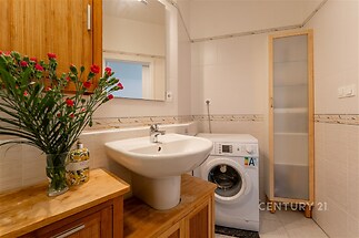 Koupelna s umyvadlem, dlažbou a pračkou, dřevěný úložný nábytek, moderní úprava, prostorný interiér.