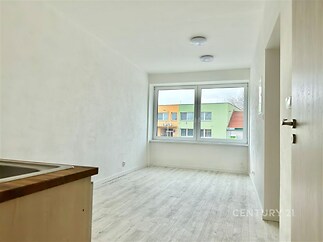 Světlý obývací pokoj s velkými okny, laminátovou podlahou a moderním designem, ideální pro útulné bydlení v rekonstruovaném bytě.
