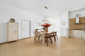 Jídelna s dlažbou, moderním nábytkem a velkými okny. Světlá místnost s elegantním designem a stylovým osvětlením.