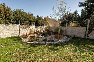 Přirozená zahrada s kamenným chodníkem a okrasnými stromy, obklopená vysokým plotem pro soukromí. Zahrada je vhodná pro relaxaci a nabízí klidné prostředí.