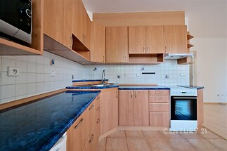 Kuchyň s dřevěnými skříněmi a modrou pracovní deskou, dlažba na podlaze, moderní spotřebiče a obkladová stěna, světlé a prostorné prostředí