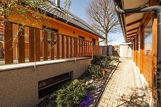 Venkovní terasa s dřevěným zábradlím a dlažbou, obklopená upravenou zahradou. Moderní exteriér domu s kvalitními materiály a výhledem na přírodu.