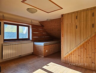 Podkrovní pokoj s parketovou podlahou a dřevěnými vestavěnými skříněmi, světlý prostor díky velkému oknu a šikmině se obložením.