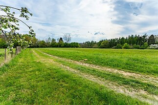 Rozsáhlý pozemek s travnatou plochou, obklopený lesy a přírodními prvky, ideální pro stavbu rodinného domu a rekreační využití.