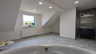 Prostorná koupelna s moderními obklady, dlažbou a vestavěným zrcadlem, disponuje vanou, světlá díky střešnímu oknu a stropnímu osvětlení.