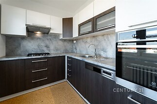 Moderní kuchyň s tmavými dřevěnými skříňkami, vestavěnou troubou a mramorovým obkladem, vybavena nerezovým dřezem a myčkou.