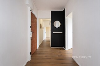 Vstupní chodba s parketovou podlahou a moderní černou stěnou, světlý prostor propojující místnosti v rekonstruovaném bytě.