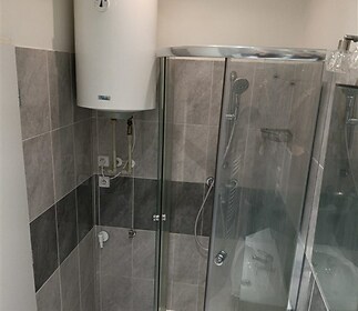 Koupelna s moderní sprchovým koutem a dlažbou, vybavená novým bojlerem a elegantními obklady, nabízí praktické využití prostoru.