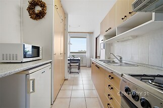 Kompaktní kuchyň s dlažbou, světlými skříňkami a spotřebiči, vedoucí do jídelního kouta s velkým oknem poskytujícím dostatek světla.