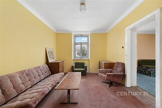 Obývací pokoj s dřevěnou podlahou, světlými stěnami a velkým oknem. Retro nábytek vytváří vintage atmosféru.